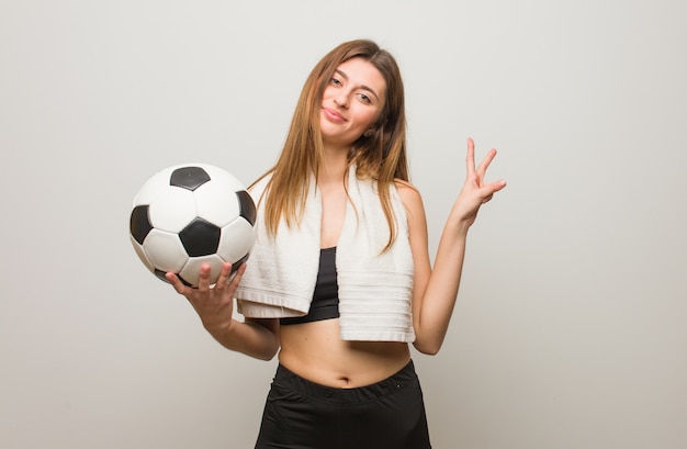 Mulher nova do russo da aptidão que faz um gesto da vitória. Segurando uma bola de futebol.