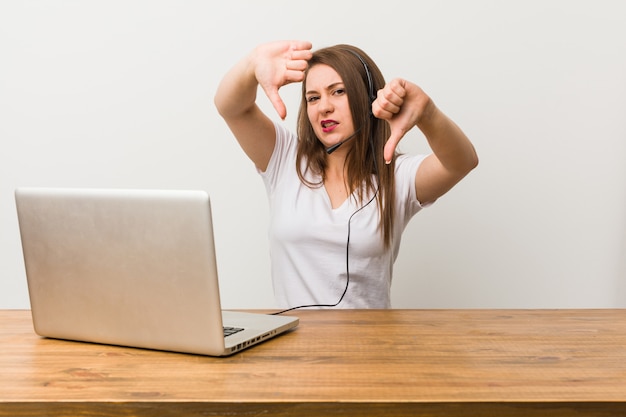 Mulher nova do telemarketer que mostra o polegar para baixo e que expressa o desagrado.