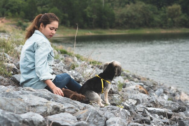 Mulher nova feliz do asain do moderno com seus cães engraçados que sentam-se na rocha ao lado do reservatório.