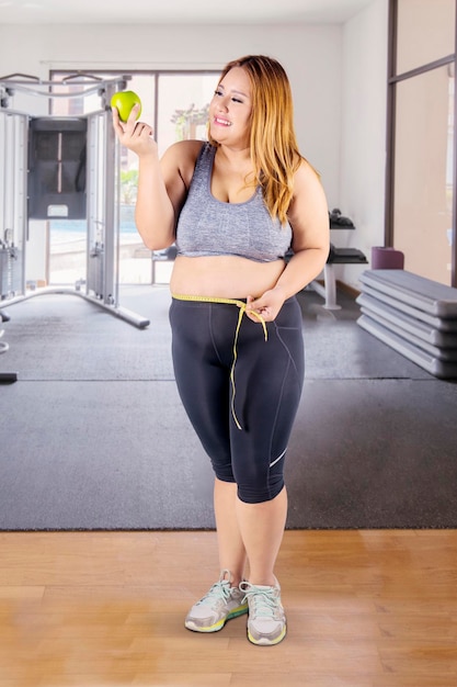 Mulher obesa com maçã e fita métrica no ginásio