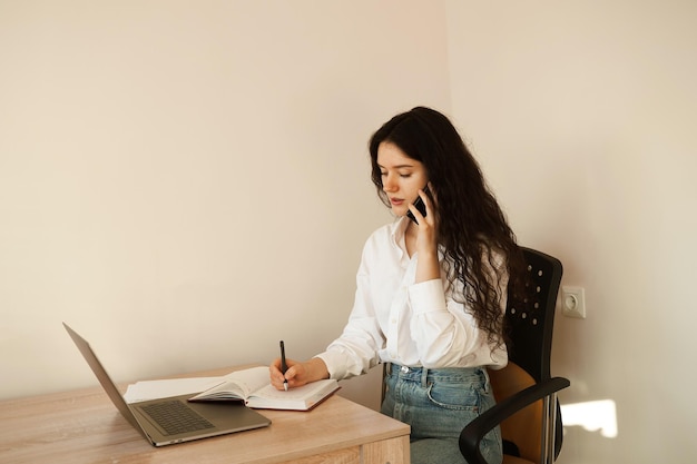 Mulher ocupada falando por telefone escreve notas no notebook e trabalhando no laptop Chefe de garota cansada trabalhando online com colegas em casa