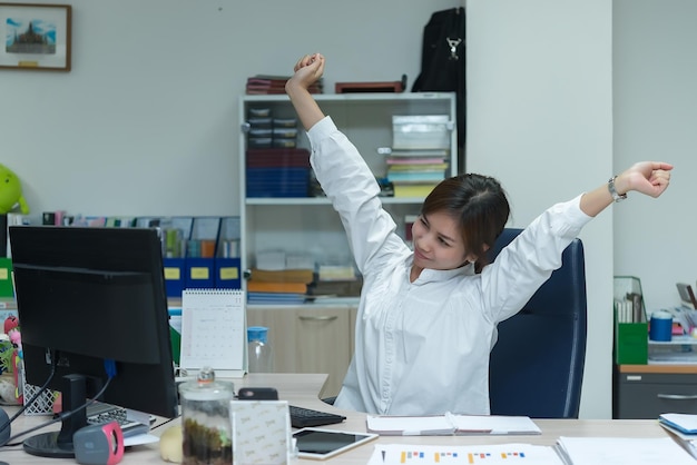 Mulher oficial asiática esticando o corpo na mesa do escritório do ângulo traseiroPovo da TailândiaEmpresária cansada do trabalho duro