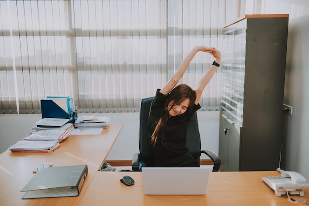 Mulher oficial asiática esticando o corpo na mesa do escritório