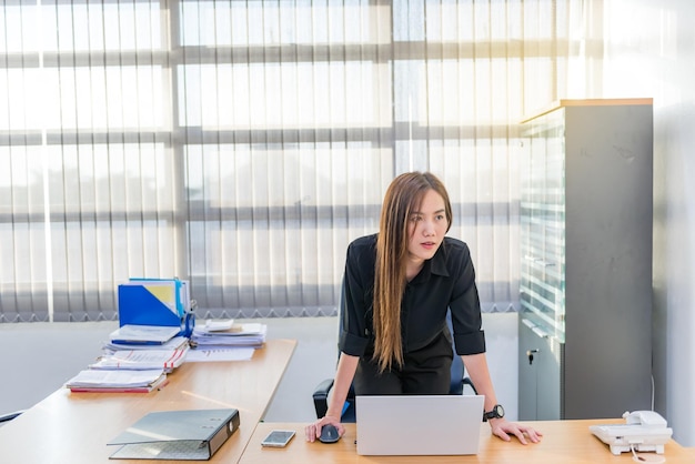 Mulher oficial asiática fica olhando o tempo na parede na mesa do escritório