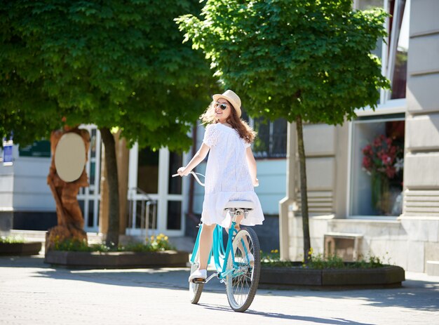 Foto mulher olha para a câmera enquanto andava de bicicleta azul no centro da cidade pavimentada