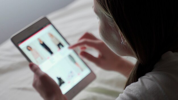 Foto mulher olha para a página do tablet. uma mulher observa as tendências da moda em um tablet. a tela está desfocada.