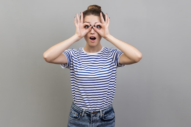 Foto mulher olhando através de binóculos gesto e expressando surpresa zoom visão explorando a distância