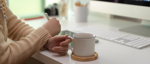 Mulher olhando no tablet e segurando a xícara de café na mesa de escritório branco