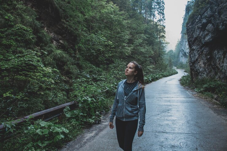 Foto mulher olhando para cima enquanto está de pé na estrada na floresta