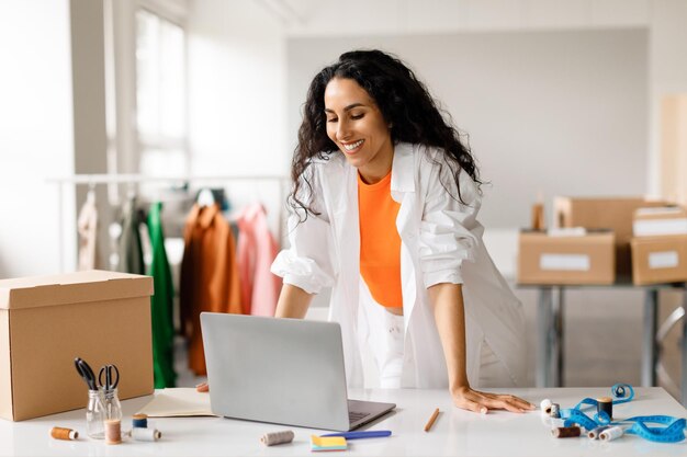 Foto mulher olhando para laptop recebendo pedidos on-line em loja de roupas