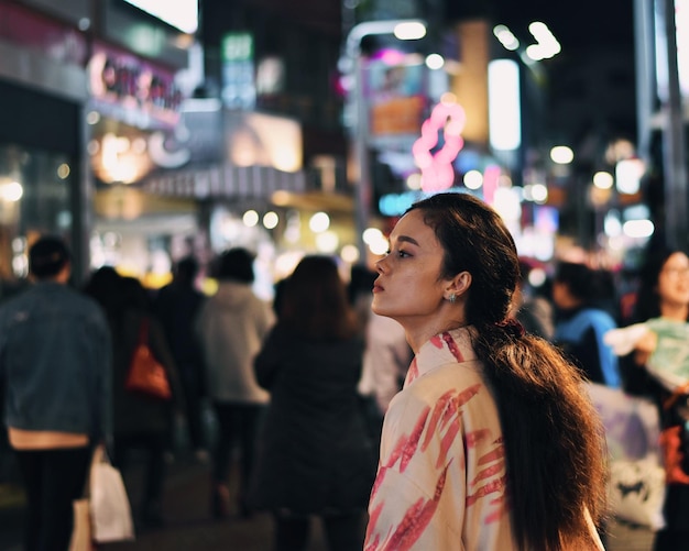 Mulher olhando para longe enquanto está de pé na cidade iluminada à noite