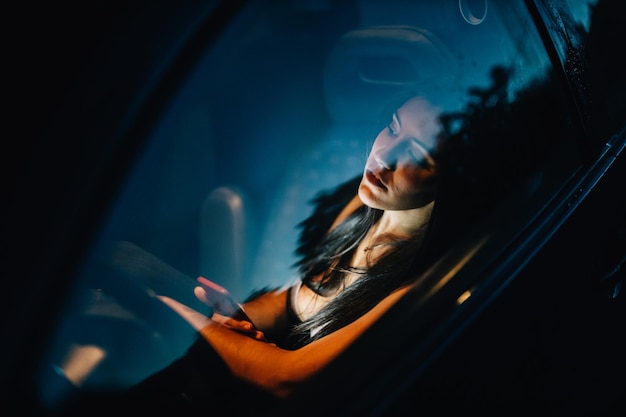 Foto mulher olhando para longe enquanto segura telefone celular visto através da janela do carro com reflexo