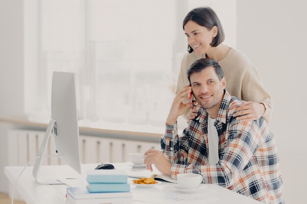 Mulher olhando para o computador enquanto o homem fala ao telefone
