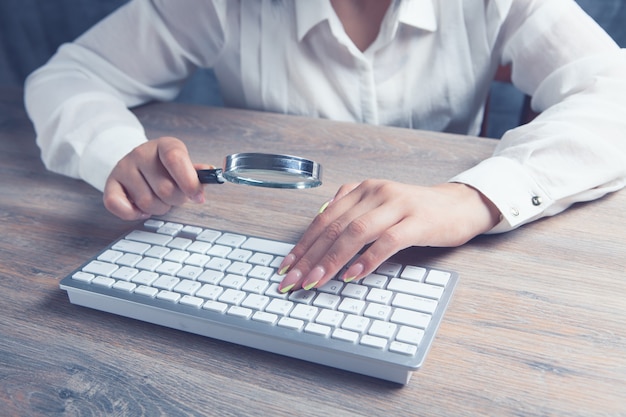 Mulher olhando para o teclado com uma lupa