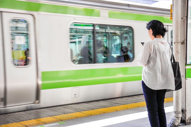 Mulher olhando para o telefone na plataforma da linha Yamanote na Estação de Tóquio