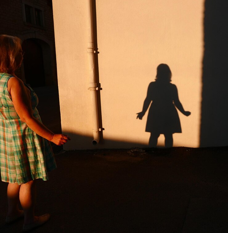 Foto mulher olhando para sua sombra na parede durante o pôr do sol