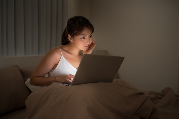 Mulher olhando para um laptop na cama