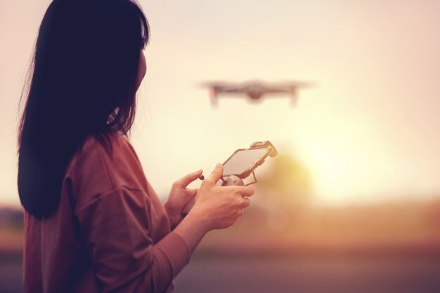 Mulher operando um drone com controle remoto ao pôr do sol