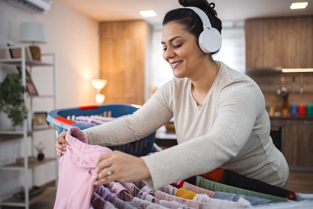 Mulher ouvindo música enquanto pendura a roupa na prateleira de secagem em casa