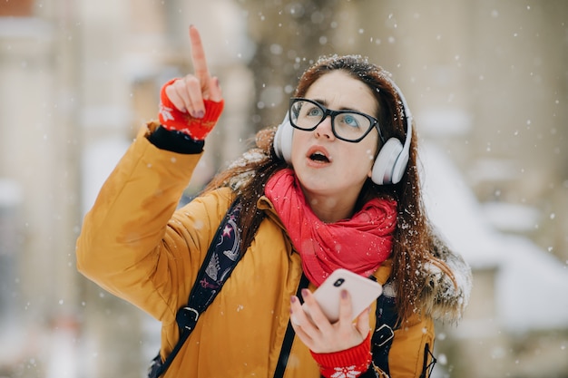 Mulher ouvindo música lá fora no inverno. Árvores na neve. Nuvem de neve do tempo