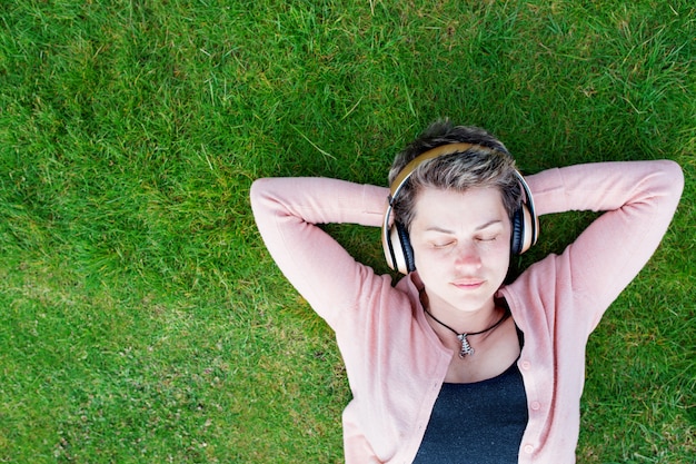 Mulher ouvindo música ou audiobook e descansando na grama verde