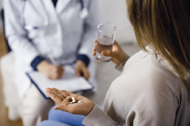 Foto mulher-paciente de close-up segurando pílulas perto de seu médico, hora de tomar medicamentos, cura para dor de cabeça ou remédios analgésicos. fique em casa durante a pandemia de coronavírus e a quarentena de auto-isolamento