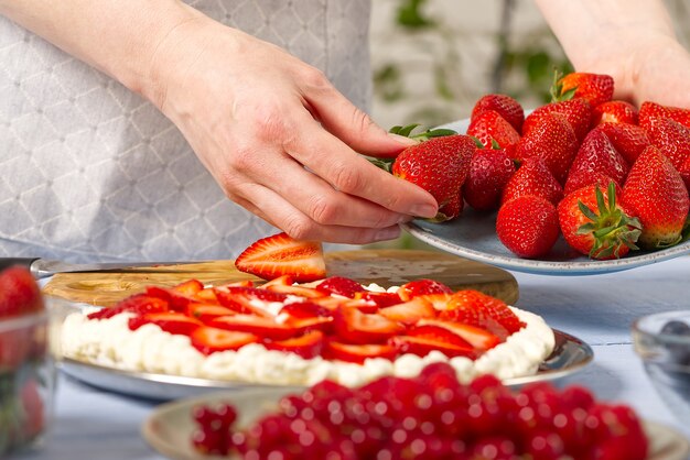 Mulher padeiro com as mãos segurando morangos para um bolo caseiro de morango feito de merengue e creme