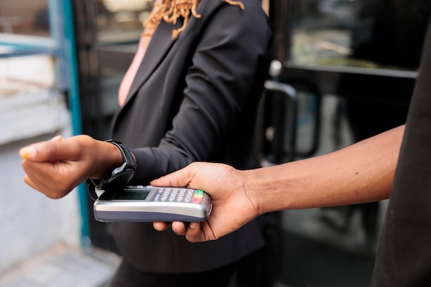 Mulher pagando com smartwatch, close-up disponível, pagamento sem contato pos, tecnologia nfc. Serviço de entrega de comida de escritório, entregador afro-americano segurando a visão de perto do terminal