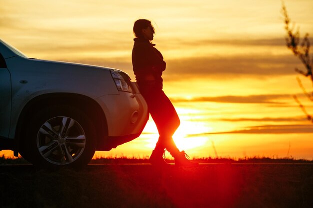 Mulher parada perto do pôr do sol do carro na viagem de fundo