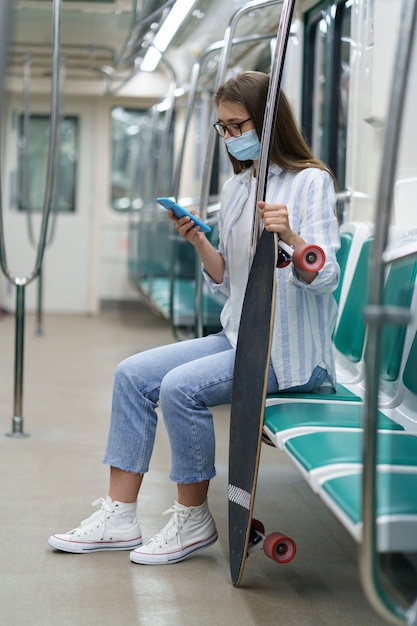 Mulher passageira da geração do milênio usando telefone celular, usa máscara facial contra cobiça no trem do metrô