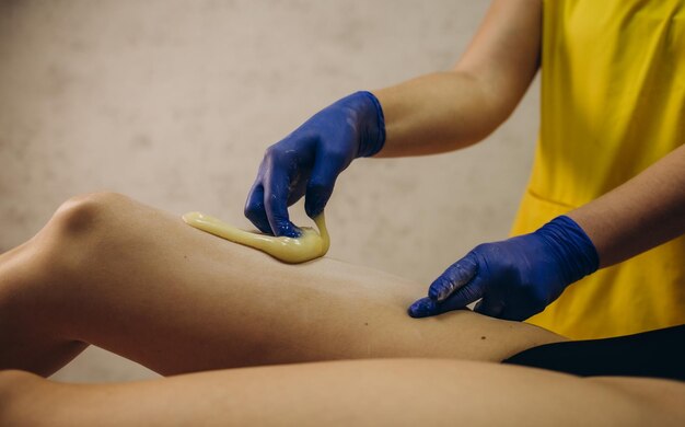 Mulher passando por procedimento de depilação na perna com pasta de açúcar no salão