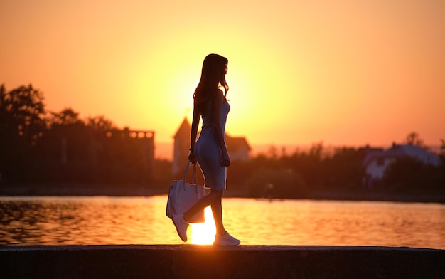 Mulher pedestre solitária andando sozinha no lado do lago na noite quente Conceito de solidão e relaxamento