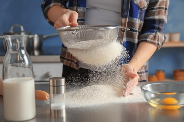 Mulher peneirando farinha na mesa da cozinha