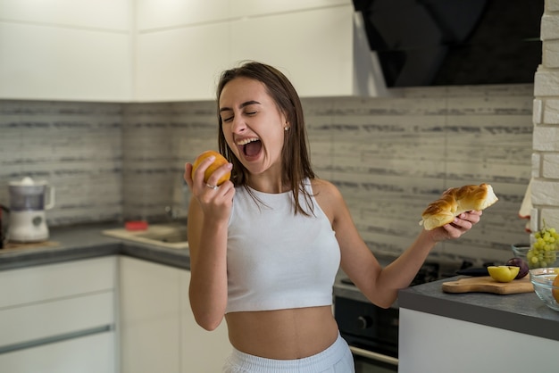 Mulher pensando no que comer no café da manhã entre frutas e pão doce