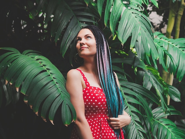 Foto mulher pensativa com dreadlocks de pé contra plantas