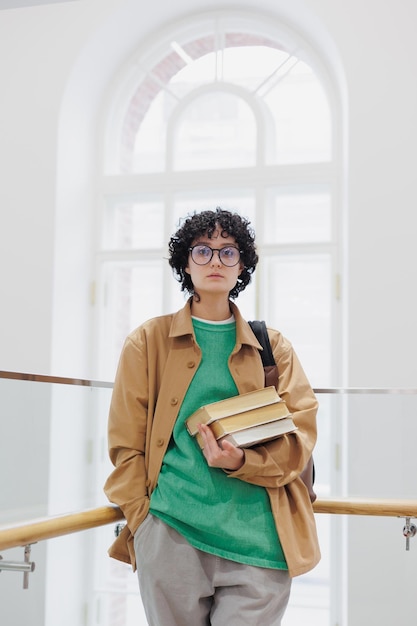 Foto mulher pensativa com pilha de livros nas mãos na biblioteca ou aluna bem-sucedida de coworking