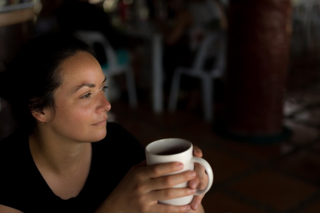 Mulher pensativa olhando para longe enquanto segura uma xícara de café