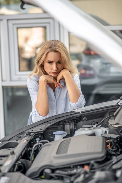 Foto mulher pensativa olhando tristemente para o capô do carro