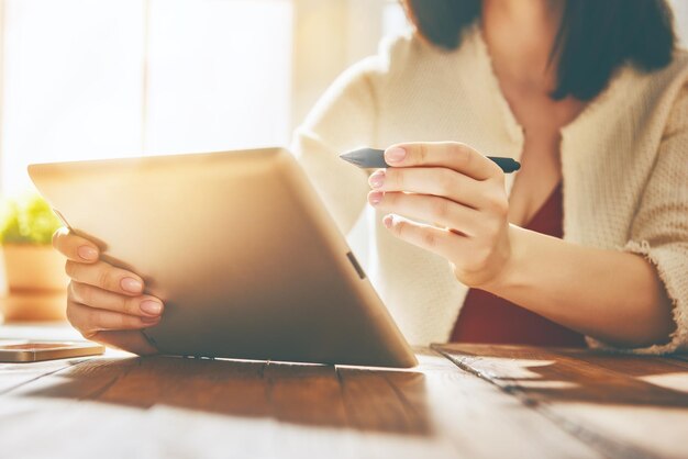 Mulher pensativa que trabalha com o tablet enquanto está sentado na mesa.