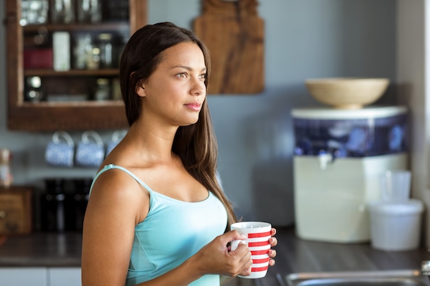 Mulher pensativa, segurando a xícara de café na cozinha