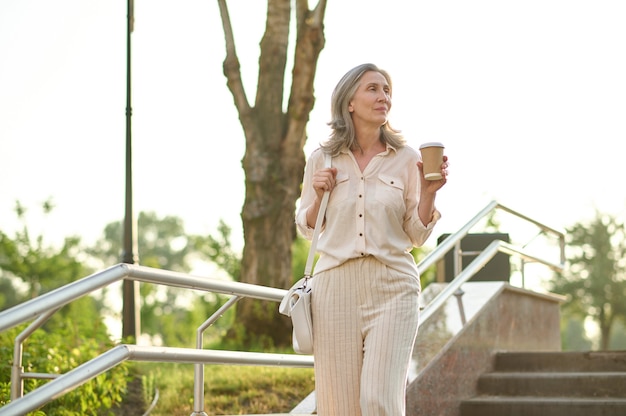 Mulher pensativa tomando café na escada do parque