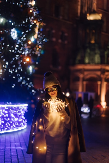 Mulher perto de uma árvore de Natal na rua com guirlandas nas mãos dela