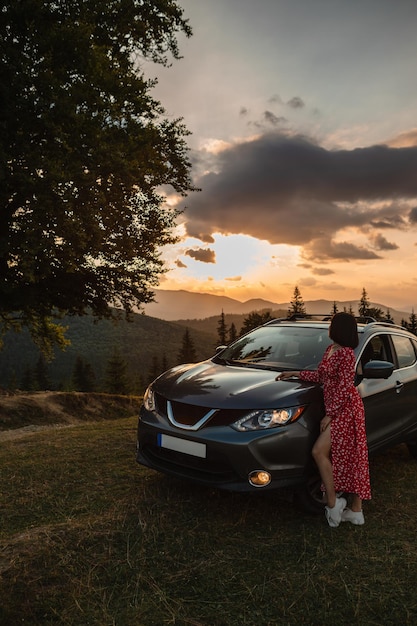 Mulher perto do pôr do sol do carro nas montanhas