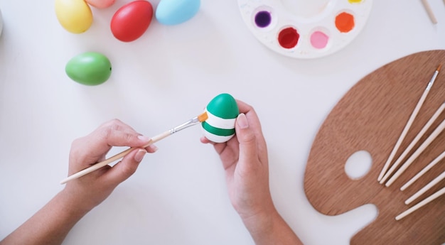 Mulher pintando ovos de Páscoa em casa, família se preparando para a Páscoa Mãos de uma menina com um ovo de páscoa