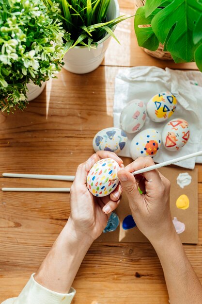 Foto mulher pintando um moderno ovos de páscoa pincéis e pinturas com flores e plantas feliz páscoa