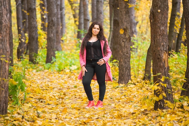 Mulher plus size de calça preta e jaqueta rosa em pé na floresta de outono