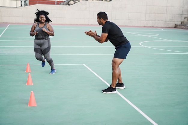 Mulher plus size e personal trainer fazendo exercícios de cone de velocidade e agilidade em sessões de treino ao ar livre