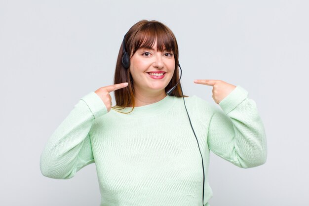 Mulher plus size sorrindo com confiança apontando para o seu largo sorriso, atitude positiva, relaxada e satisfeita