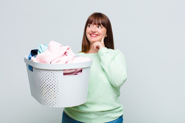 Mulher plus size sorrindo feliz e sonhando acordada ou duvidando, olhando para o lado