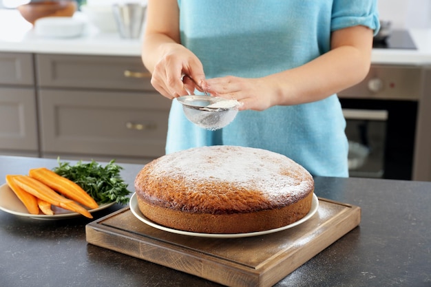 Mulher polvilhando bolo de cenoura fresco com açúcar de confeiteiro na mesa